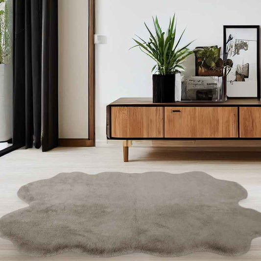 A modern shaped luxury faux fur rug in a natural color, displayed on the floor in a room with wooden furniture and black curtains.